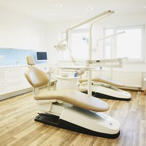 Moderner Zahnarztpraxisraum mit Behandlungsstuhl, Computern und heller Einrichtung.