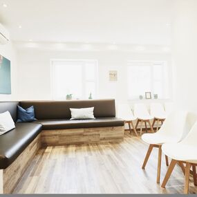 Heller, moderner Wartebereich mit Sitzbank, weißen Stühlen und Holzfußboden.