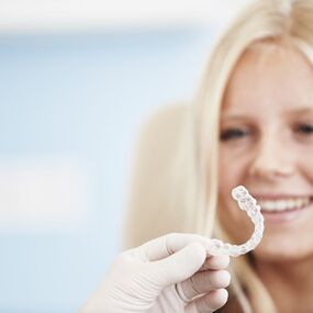 Junges Mädchen lächelt beim Zahnarzt, der eine durchsichtige Zahnschiene präsentiert.