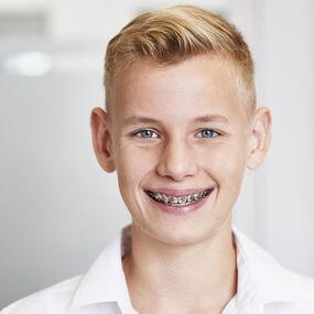 Junger Teenager mit Zahnspange lächelt in einer modernen Zahnarztpraxis.