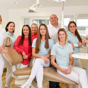 Team einer Zahnarztpraxis steht gemeinsam im modernen Behandlungszimmer und lächelt.